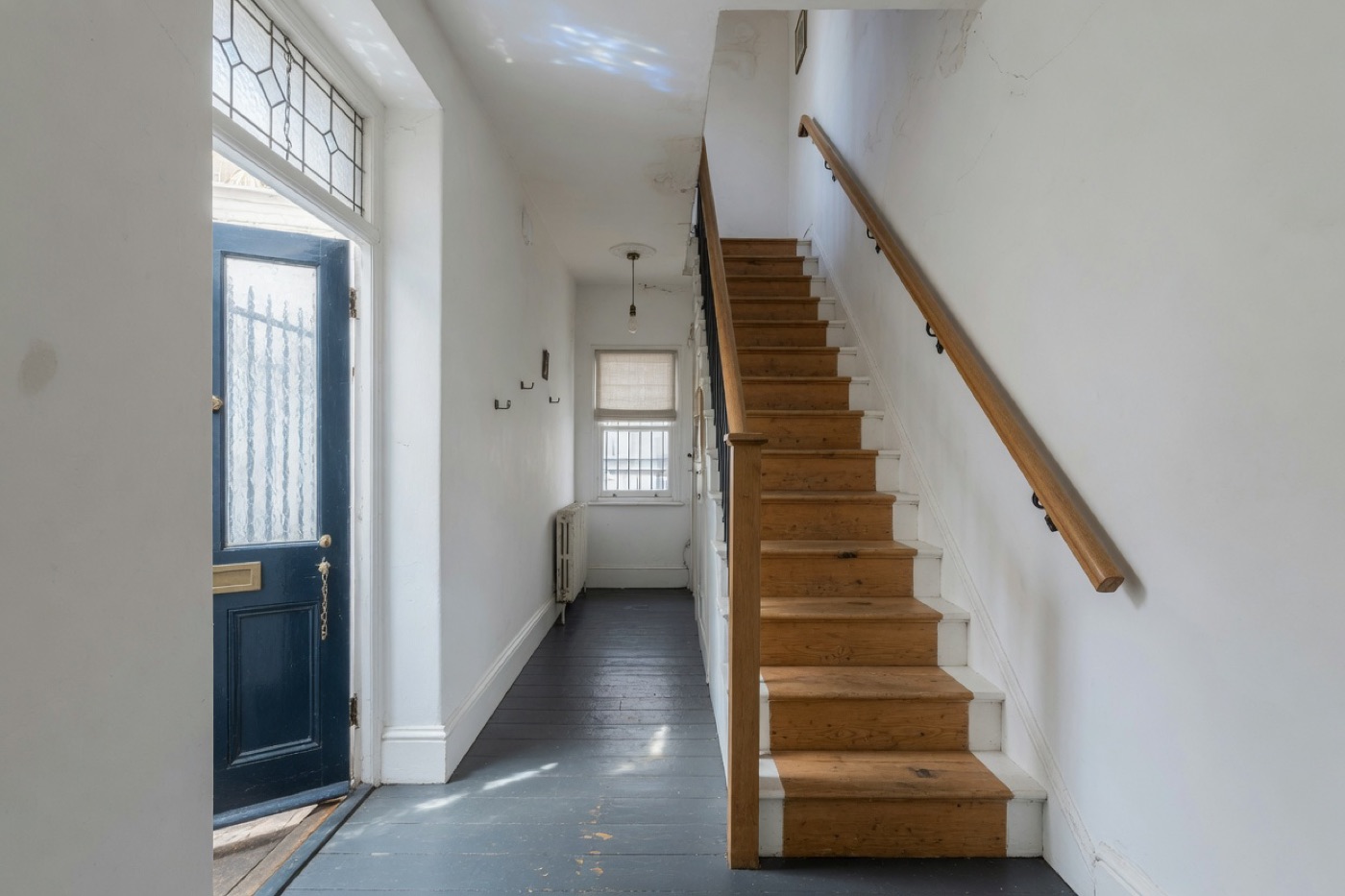 A terrace hallway with oak stair treads, a timber handrail, and a blue front door.